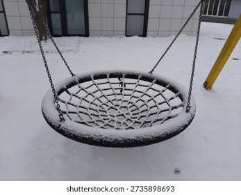 Empty rope swing covered with snow in a winter park or forest
Close-up of a handmade rope swing hanging on a tree branch during snowfall. Winter landscape with snowy woods on the background. Concept of nostalgia, winter season, and cold weather.