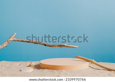 Empty round beige platform podium and dry tree twigs on white beach sand background. Minimal creative composition background for cosmetics or products presentation with blue background. Front view
