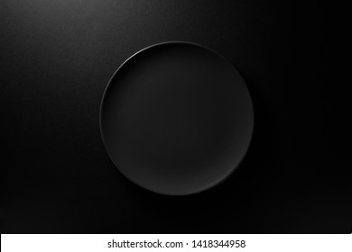 Empty Round Black Plate On Dark Moody Black Background With Copy Space. Overhead View 