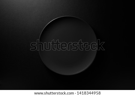 Empty round black plate on dark moody black background with copy space. Overhead view 