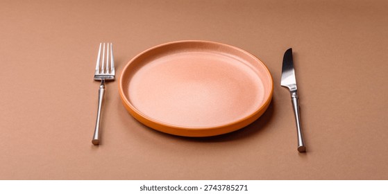 An empty round ceramic plate, knife, and fork as a dining table setting. An empty plate as a backdrop for your design