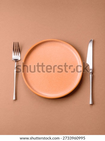 An empty round ceramic plate, knife, and fork as a dining table setting. An empty plate as a backdrop for your design