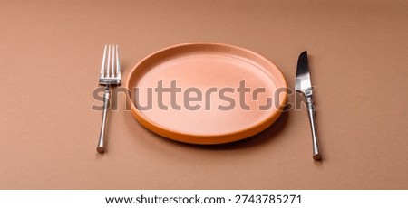 An empty round ceramic plate, knife, and fork as a dining table setting. An empty plate as a backdrop for your design