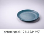 Empty round ceramic plate on a plain background, flatley with copy space. Kitchen utensils in home kitchen