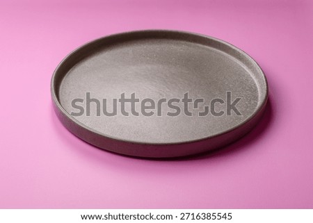 An empty round ceramic plate on a pink background as a kitchen utensil. An empty plate as a food background for your design