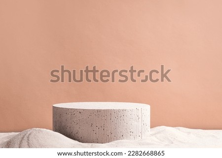 Empty round concrete platform podium on beach sand and beige background. Minimal creative background for cosmetics or products presentation. Front view, copy space.
