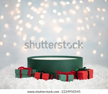 Empty round gift box in the snow on a blue background with bokeh. Christmas background for design. Image for montage or display your products. New Year red and green gifts. Copy space. Side view.
