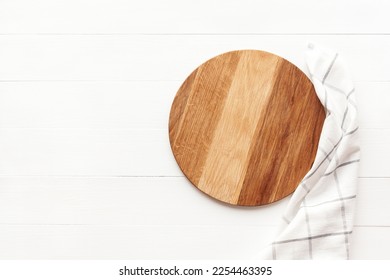 Empty round wooden cutting board with kitchen towel on white table. Round cutting board or serving tray mockup. Copy space, flat lay, top view. - Shutterstock ID 2254463395