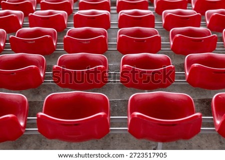 Empty rows of red plastic stadium seats create a repetitive pattern in a vacant sports arena before an event