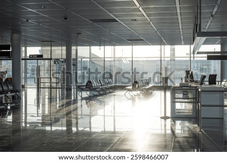 Empty rows of seats and benches inside international airport terminal. Departure waiting room near gate. Large windows, natural light, no people.