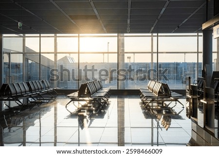 Empty rows of seats and benches inside international airport terminal. Departure waiting room near gate. Large windows, natural light, no people.
