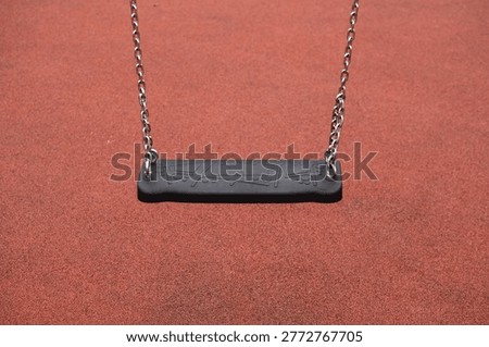 Empty rubber swing with metal chains on red playground surface