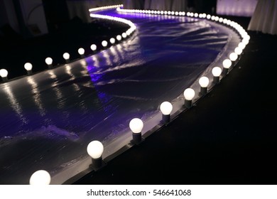 Empty Runway Fashion Show with Ball glowing lighting along walk way with plastic white floor in the dark
