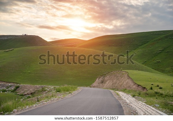 Empty rural road in\
mountain ranges in sunrise morning,curvy road leading through up\
the mountains,gentle and soft greensward covered on hills with\
people and car in distant