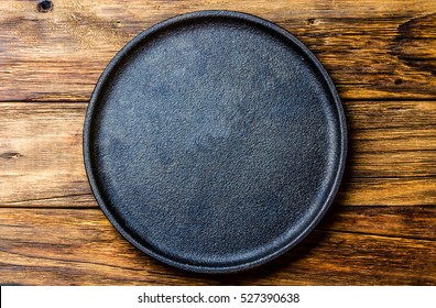 Empty Rustic Black Cast Iron Plate Over Old Wooden Background. Top View