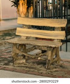 Empty rustic concrete park bench designed like wood logs on an interlocking pavement walkway outdoors.