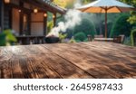 Empty rustic wooden table with copy space in sunny summer garden with small garden house background. Outdoor party, grilling time, summer relaxation concept. Mockup for food drink or seasonal product.