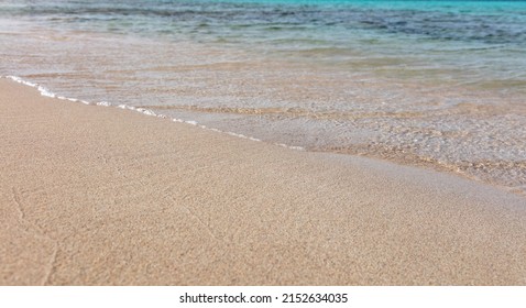 Empty sandy beach in Greece, close up view. Sea water touch wet white sand, view from above, copy space. Sunny day, summer holiday, Greek island.