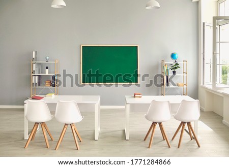 Empty school classroom interior with desks and chairs, space for text on chalkboard. Modern schoolroom with furniture