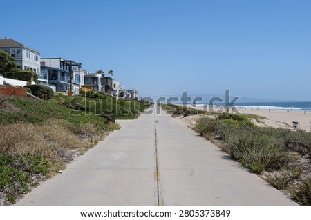 Empty section of The Strand boardwalk and Marvin Braude Bike Trail leading towards Hermosa Beach Pier, with luxury houses on the left and the ocean on the right, Los Angeles