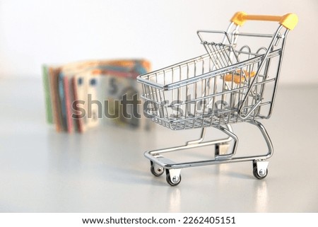 Empty shopping cart and money, several euro banknotes on white background. Conceptual image about purchasing power, family expenses, essential goods, consumer society. Foreground in focus. Copy space Foto stock © 