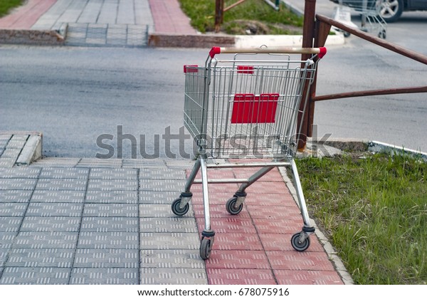 An empty shopping cart from a supermarket in red,\
abandoned on the street.