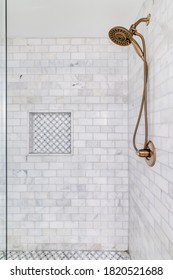 An Empty Shower With Subway Tiles And Small Ceramic Tiles On The Floor And Shelf With A Gold Shower Head.