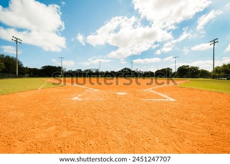 An empty softball field under scattered clouds