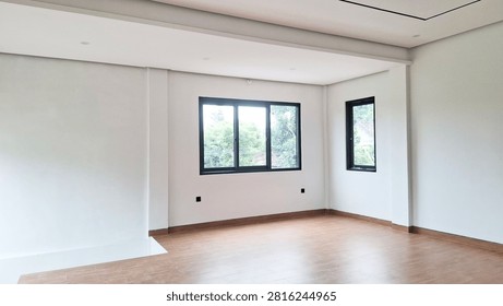 The empty space of the apartment features high ceilings, aesthetic wood floors, crisp white walls, and large glass windows for natural light and a view of the greenery