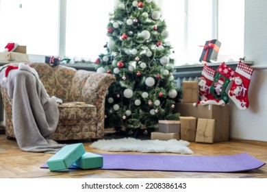 Empty Space In Fitness Center With Big Windows And Natural Wooden Floor. Unrolled Yoga Mat On The Floor, No People. Decorated Christmas Tree.