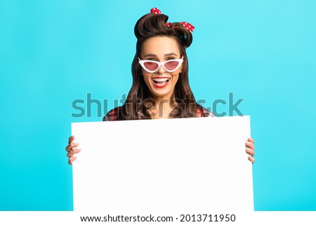 Empty space for text and ad, awesome promo, best offer. Shocked pinup woman in retro wear presenting something on white blank poster over blue studio background, mockup