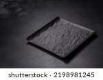 Empty square black plate over dark slate. Aerial view, with copy space