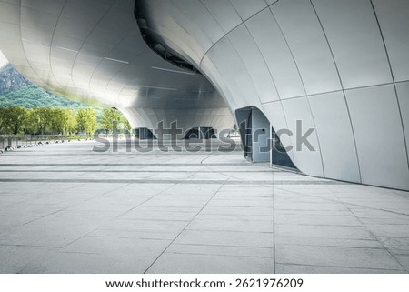 Empty square floor in front of a modern futuristic architectural building facade with green mountain background.