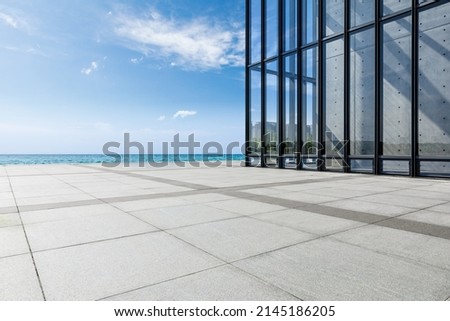 Empty square floor and glass wall building with lake under blue sky