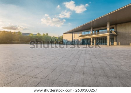 Empty square paved floor in front of a modern concrete building exterior with trees at sunrise.