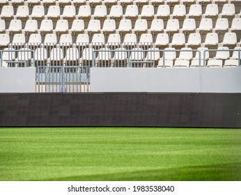 Empty stadium with white chairs in tribune and the green lawn grass - Shutterstock ID 1983538040