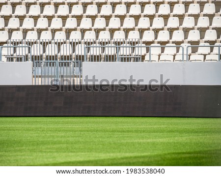Empty stadium with white chairs in tribune and the green lawn grass