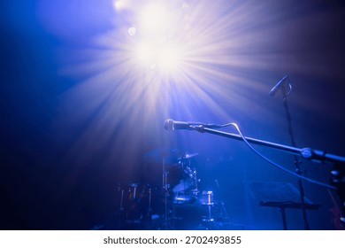 Empty stage with musical instruments and selective focus on microphone under blue concert lighting. Scene captures atmosphere of soundcheck, concert preparation, and performance setup before show.
