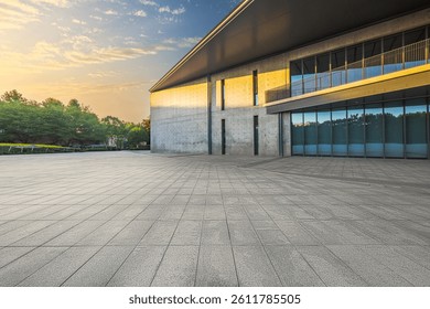 Empty stone paved square floor in front of modern concrete building exterior with large windows during sunrise.