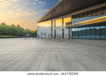 Empty stone paved square floor in front of modern concrete building exterior with large windows during sunrise.