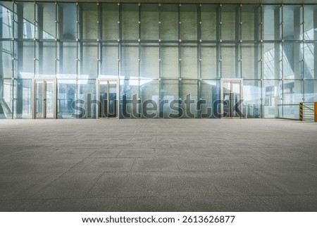 Empty stone pavement ground in front of modern building exterior with large glass wall facade.