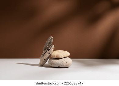 Empty stone podium with lights and shadows on brown background. Minimal backdrop. Round natural rock and piece of driftwood. Abstract pedestal or showcase for presentation. Minimal wabi sabi concept. - Shutterstock ID 2265383947