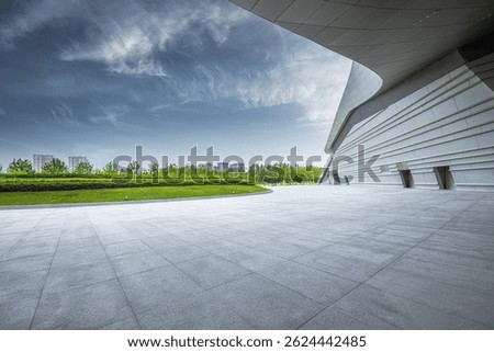 Empty stone square in front of a modern building with a green park.