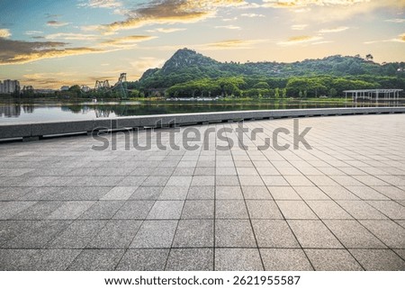 Empty stone tile floor and tranquil lake with green mountain reflection under a beautiful sunset sky.