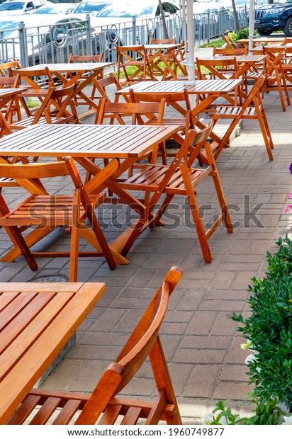 Empty street cafe with empty wooden tables against\
the backdrop of a city street with passing cars. Vertical image,\
copy space.