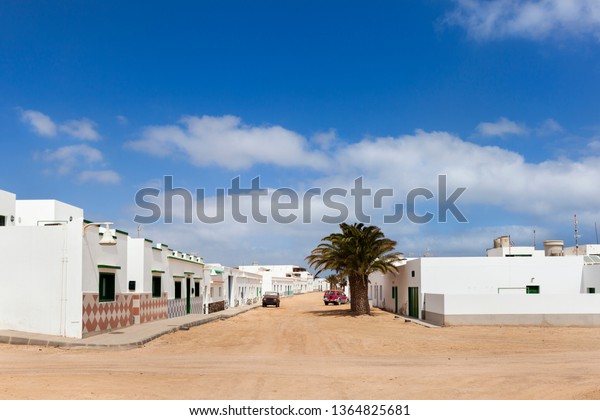 Empty street with\
sand and white houses and a palm tree in Caleta de Sebo on the\
island La Graciosa of\
Lanzarote