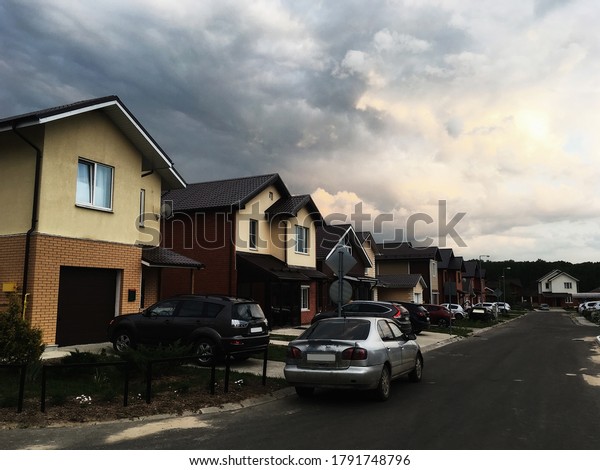 An empty street in the village. People stay\
home because of coronavirus (COVID 19) outbreak. Self-isolation\
(quarantine) in Moscow region, Russia. Brick houses, cottages, cars\
close-up. Dramatic sky