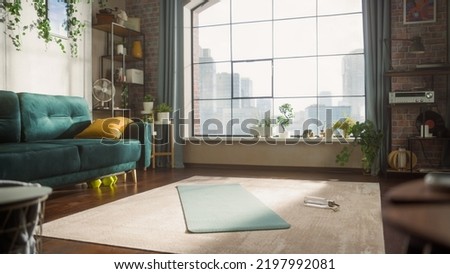 Empty Stylish Loft Apartment With Big Window. Sun Shinning on Spacious and Bright Living Room With Yoga Mat and Bottle of Water Laying on the Floor. Preperation For Online Workout Concept.
