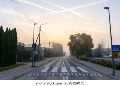 Empty suburban road at sunrise with fog, pedestrian crosswalk, and power lines in small town. Concept for urban infrastructure, road safety and traffic organisation. High quality photo - Powered by Shutterstock