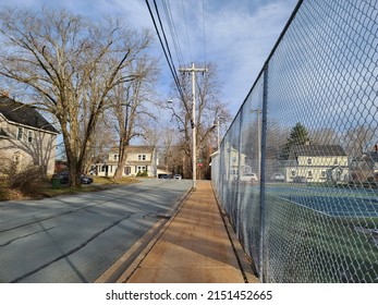 An Empty Suburban Street Along A Sidewalk With A Fence Along The Other Side.